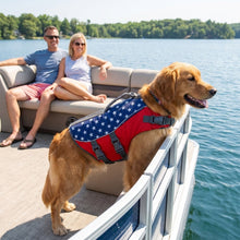 Load image into Gallery viewer, Dog wearing a life jacket with American flag design on a boat with a couple in the background.
